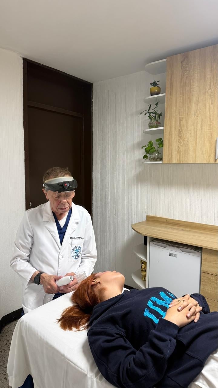 Doctor in white coat wearing headlamp examining patient lying on medical table in clinic room